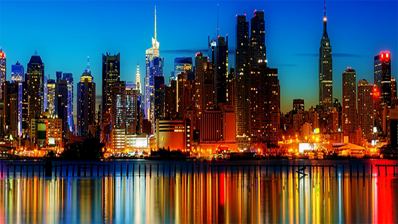 صویر مجسمه آزادی در بندر نیویورک با آسمان آبی و منظره شهری و مکان های دیدنی