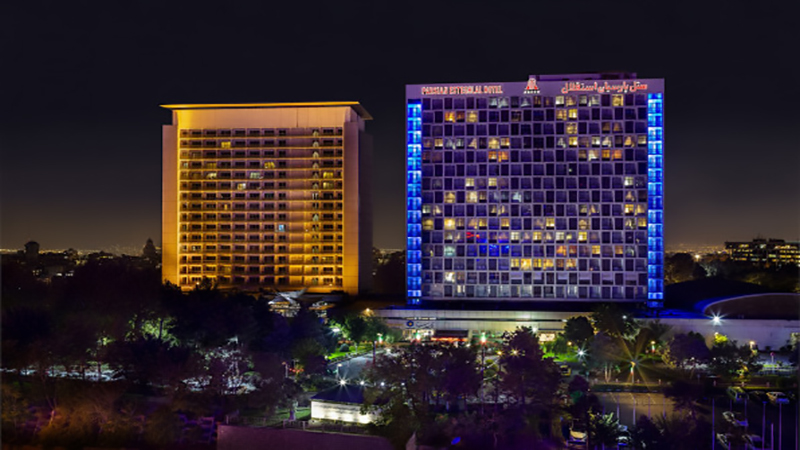 نمای شب هتل پارسیان استقلال تهران (Parsian Esteghlal Hotel Tehran) با نورپردازی طلایی و چشم‌انداز کوه‌های البرز